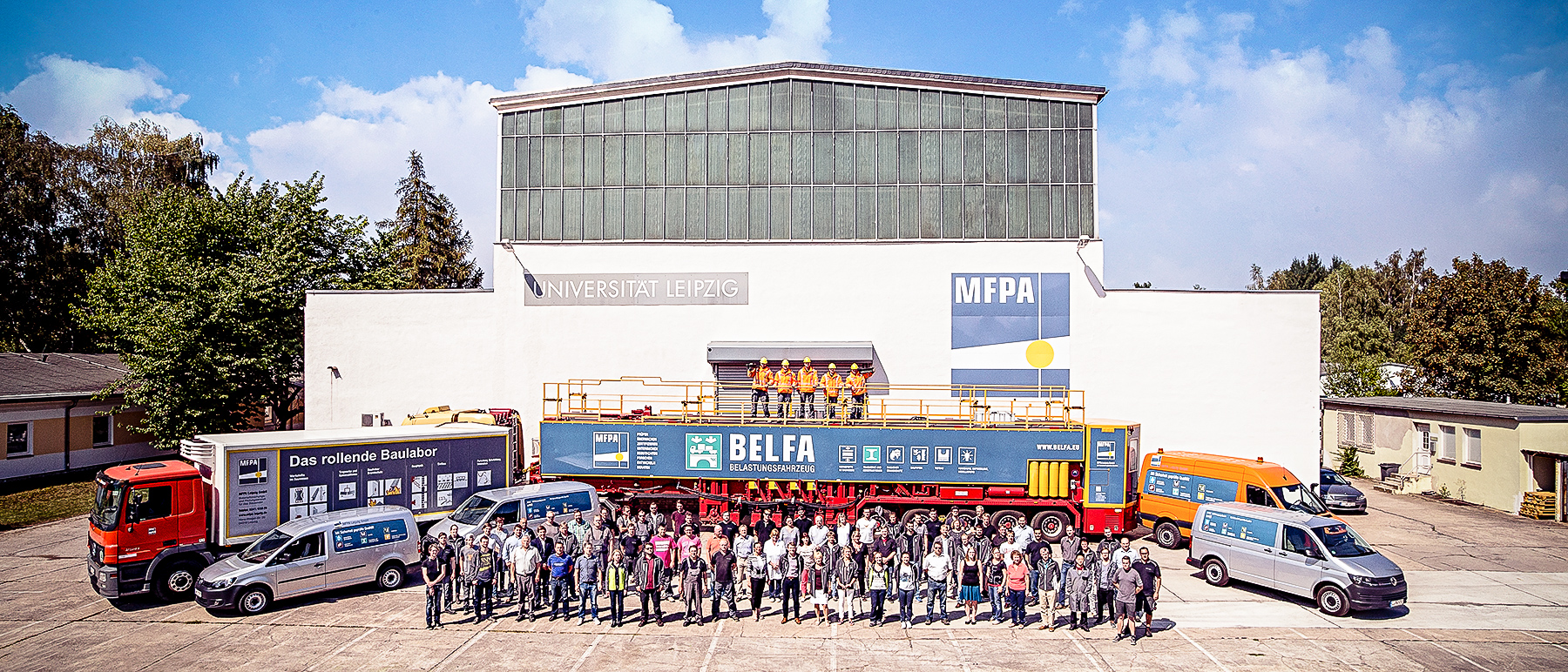 Foto aller Mitarbeiter vor dem Fuhrpark und einer Prüfhalle der MFPA Leipzig