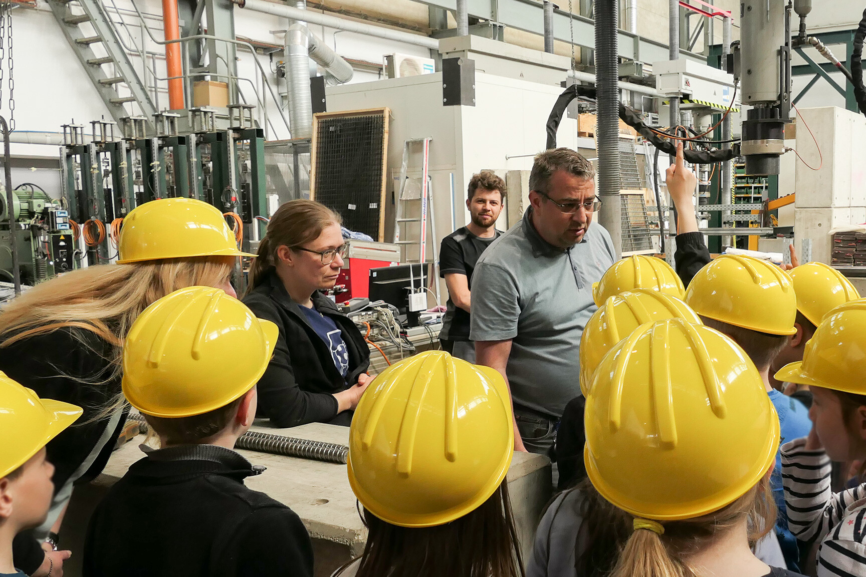 Hortkinder mit gelben Bauhelmen vor Prüfgeräten bekommen eine Erläuterung durch Ingenieure