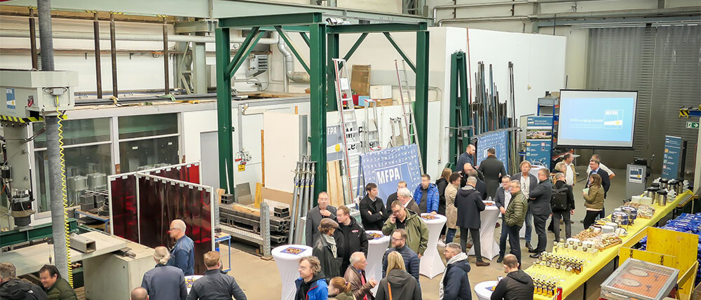 Menschen in der Prüfhalle der MFPA Leipzig an Stehtischen vor einer Präsentation